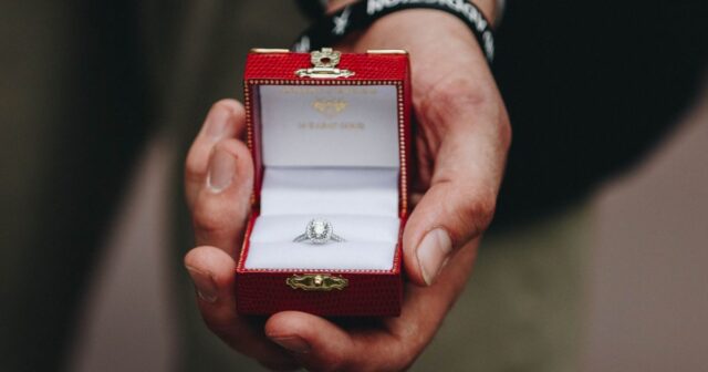 A hand holding a ring box with a diamond ring in it