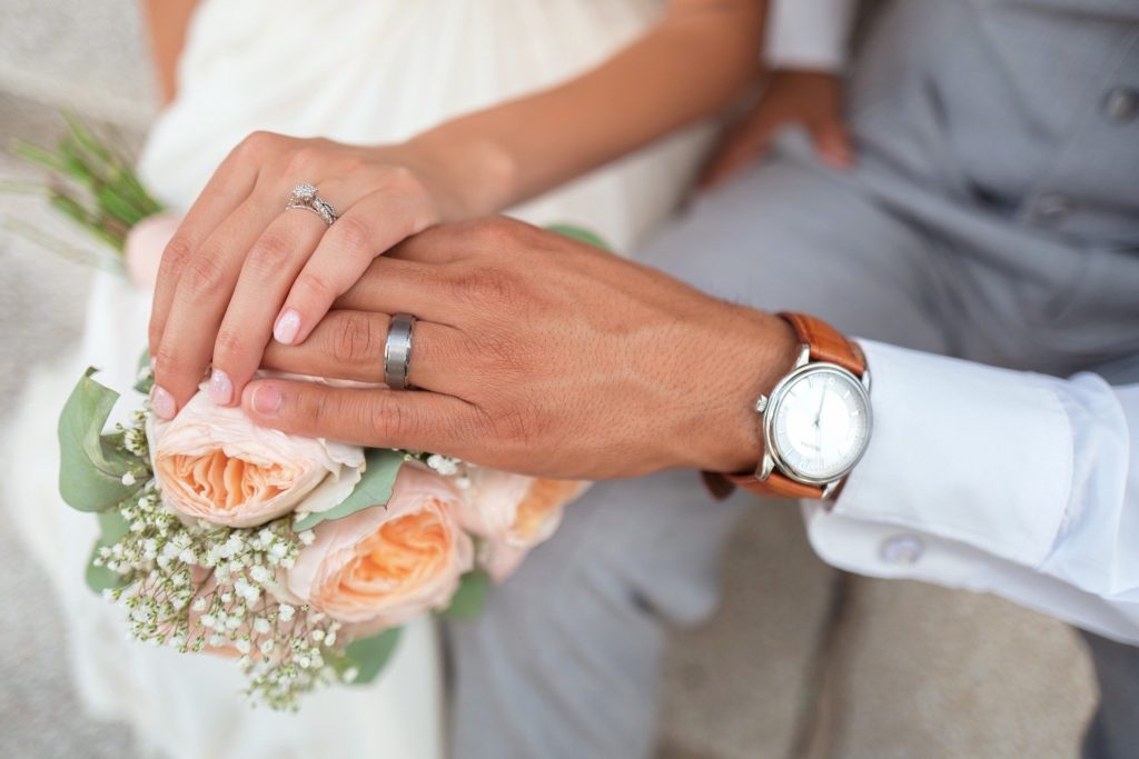 A bride couple who wearing wedding bands together and both hands on a bouquet