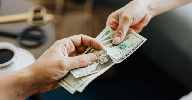 A hand passing dollars to another hand