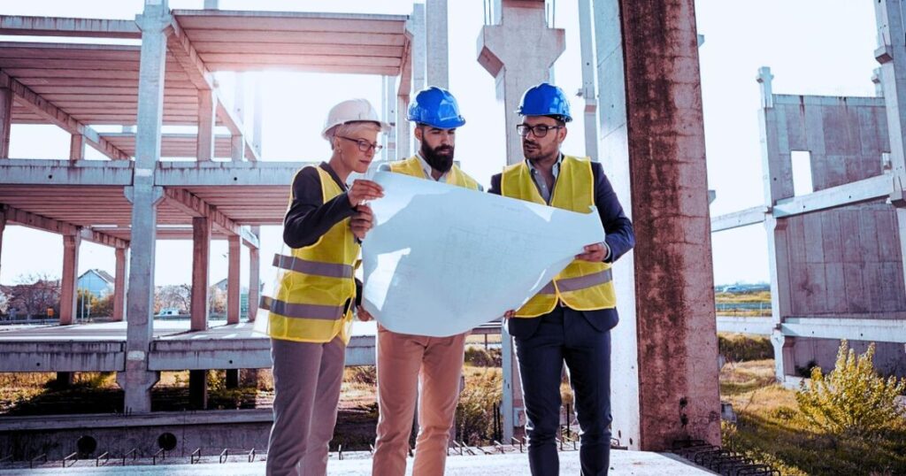 3 persons looking at the blueprint of construction, standing in front of construction site